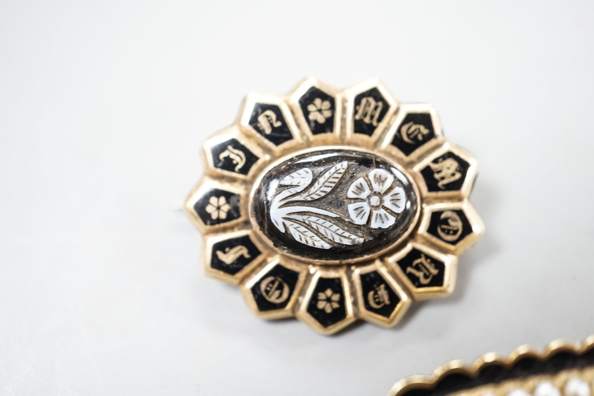 Two 19th century yellwo metal mourning brooches, one with plaited hair, split pearls and engraved inscripotion, the other with sardonyx centre stone, largest 27mm.